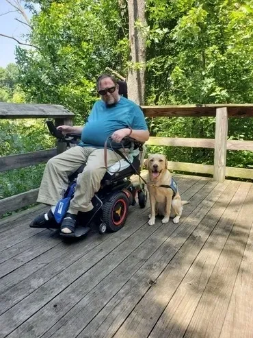 A man in a wheelchair with his dog on the deck.